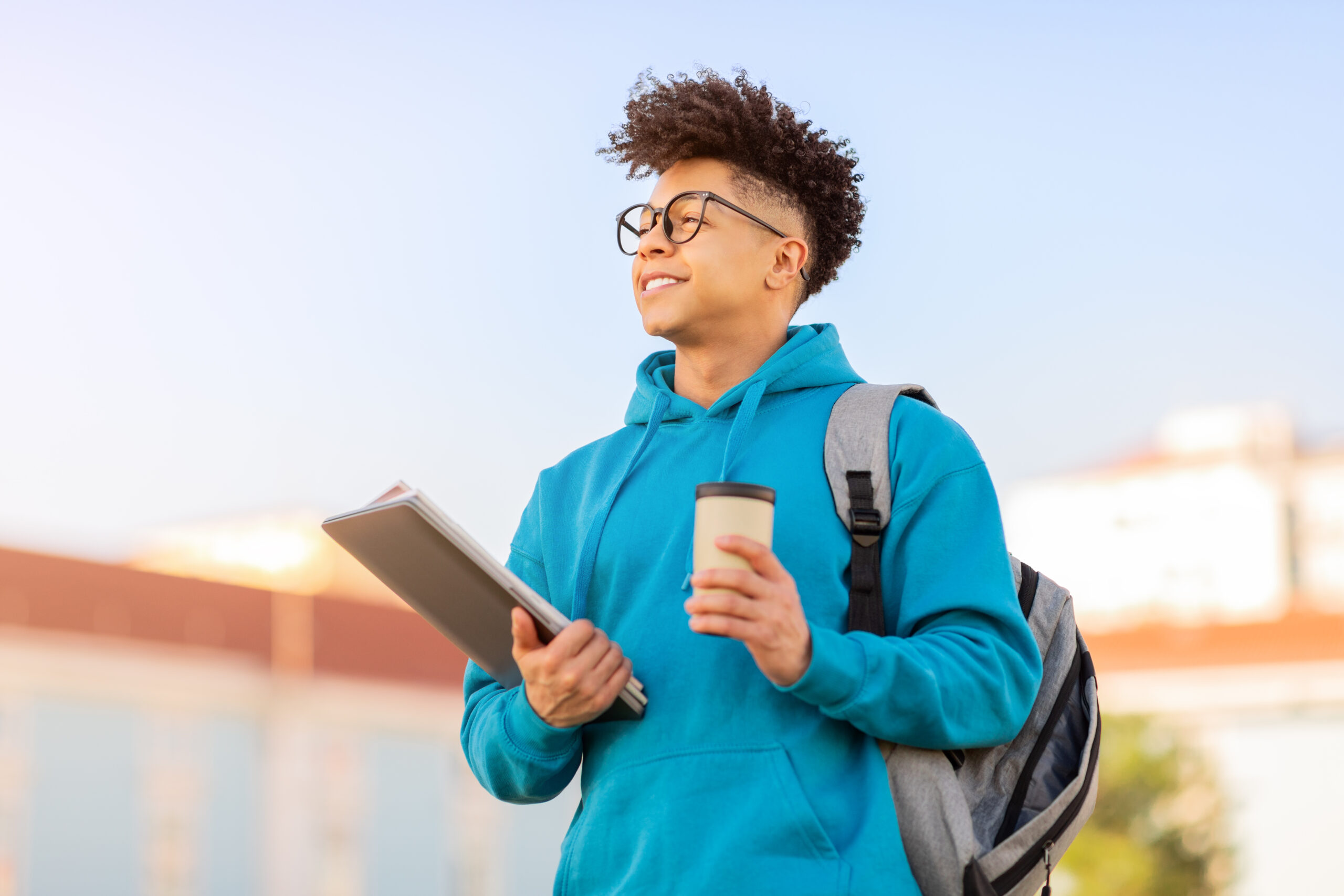 Modern Education. Young African American male student embraces education, standing outdoors with laptop and takeaway coffee. Portrait of modern learner enjoying campus lifestyle