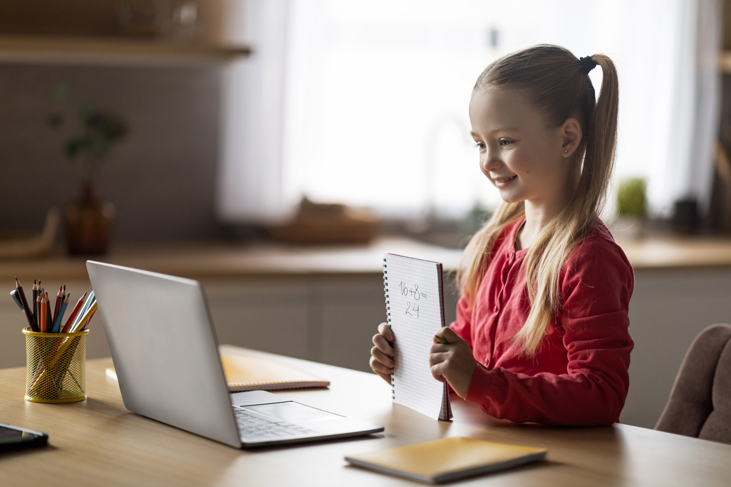 Online Math Lessons. Smiling Little Girl Having Video Call With Mathematics Teacher, Cute Preteen Schoolgirl Using Laptop At Home, Showing Task Answer In Workbook, Learning Numbers Addition